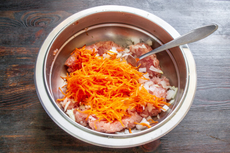Grating carrots to add sweetness and moisture to the filling. A fresh carrot being grated on a box grater.
