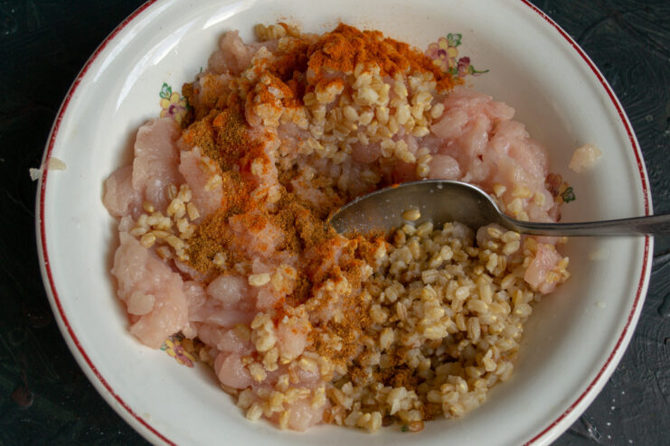 A bowl with minced chicken and cooked spelt being mixed together for the filling.