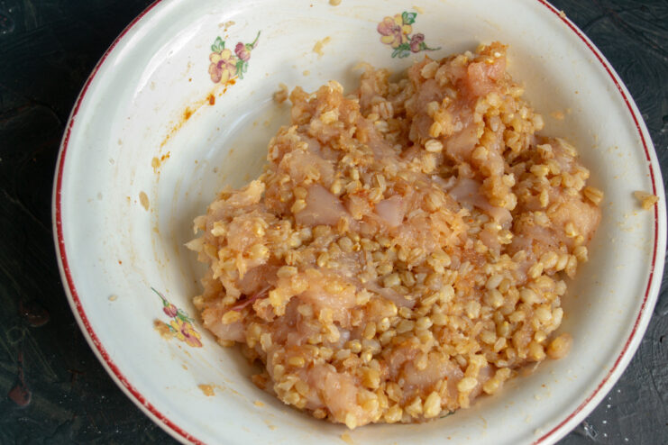 Hands mixing the chicken and spelt filling in a glass bowl until well combined.