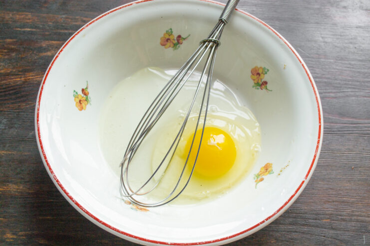 Creating the Egg Mixture for the Sandwiches A chicken egg being whisked in a white bowl to create a smooth base.