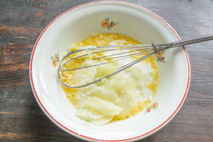 Combining Onion with the Egg and Milk Base Finely chopped onion being added to the liquid mixture in a bowl.