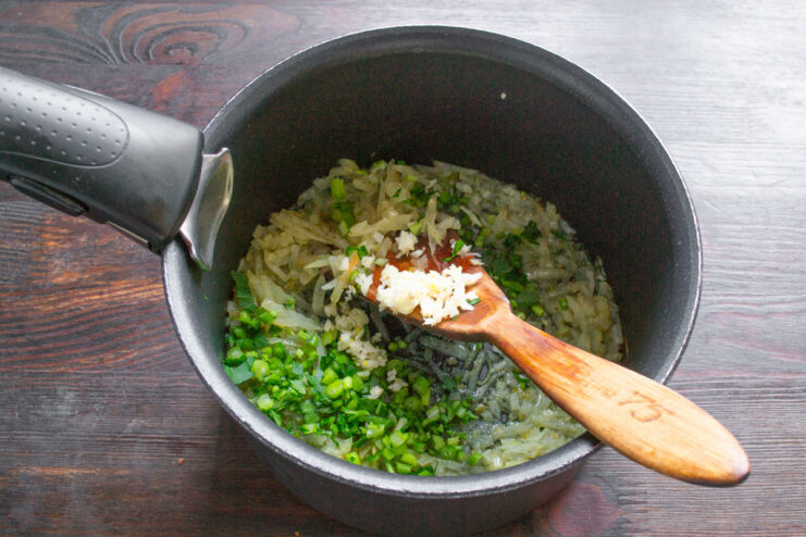 Adding Herbs and Garlic to Sautéed Onions Chopped herbs and garlic being added to sautéed onions in a pot.
