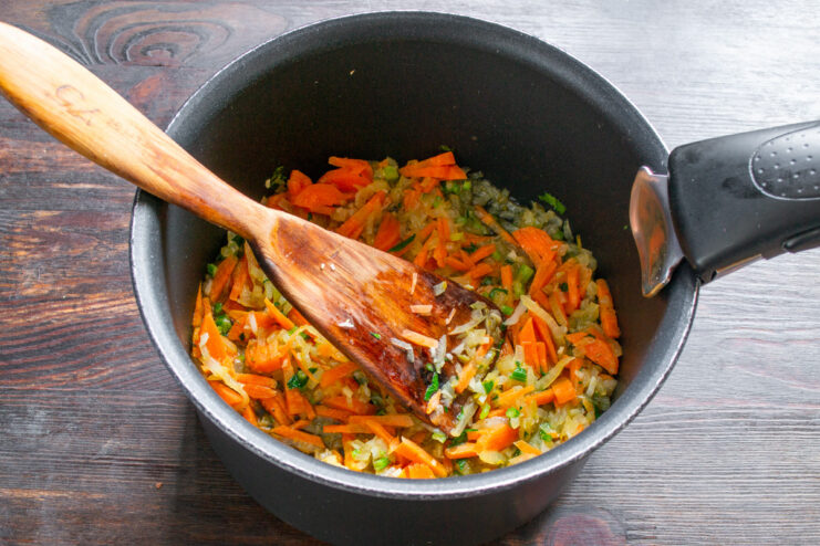 Adding Carrots to the Pot Julienned carrots being added to the pot with sautéed onions and herbs.