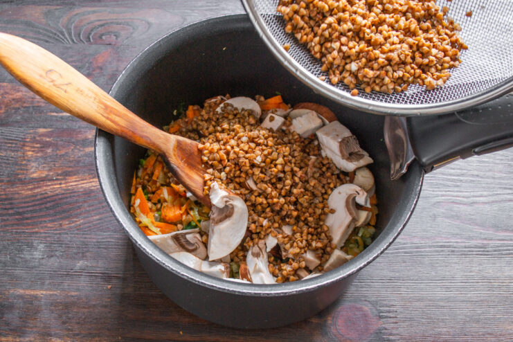 Adding Rinsed Buckwheat to the Pot Rinsed buckwheat groats being poured into the pot with vegetables and mushrooms.