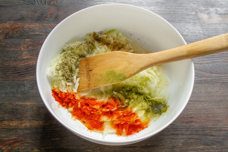 Seasoning the Onions with Aromatic Spices Spices like paprika and dried herbs being added to the chopped onions in the baking dish.