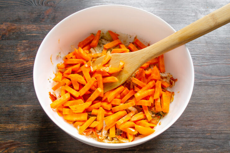 Adding Sweetness and Color with Fresh Carrots Carrot sticks being added to the baking dish with onions and spices.