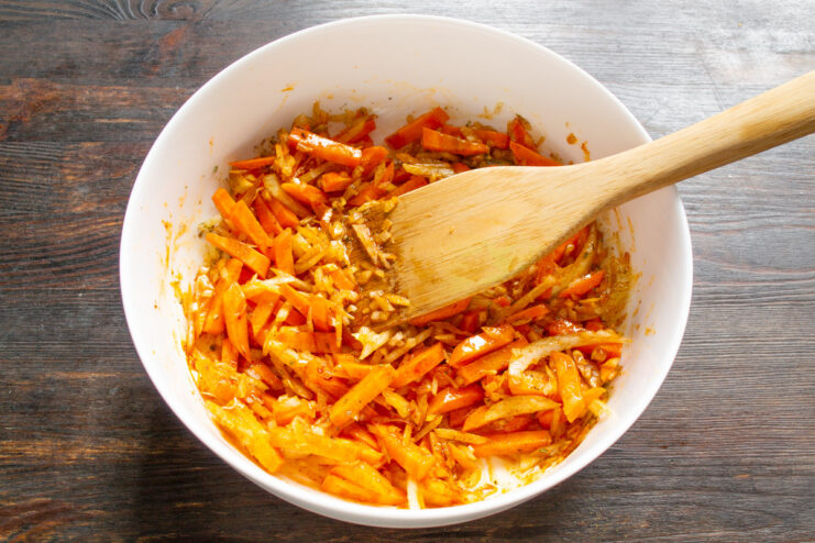 Mixing the Vegetables, Oil, and Spices for an Even Flavor A close-up of carrots and onions mixed with oil and spices in a glass baking dish.