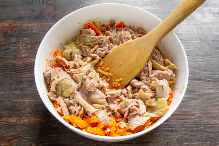 Layering the Chicken Tushenka for a Rich, Meaty Flavor Canned stewed chicken (tushenka) layered over seasoned vegetables in the baking dish.