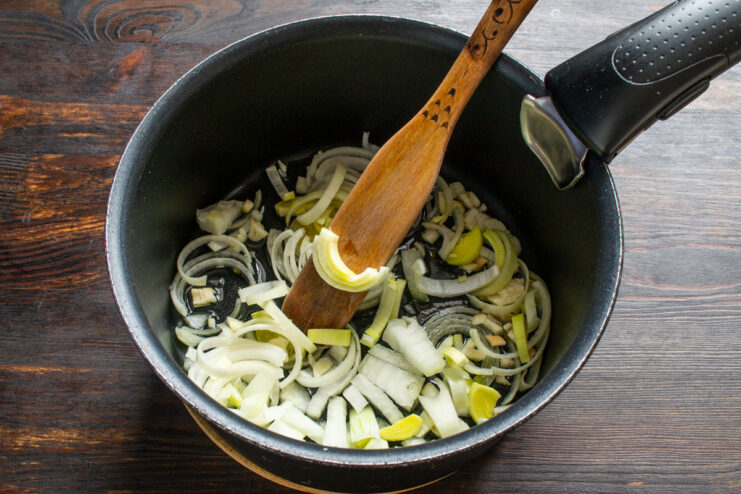 Sautéing aromatics: Start with garlic, then add leeks and onions to build the soup's flavor base. Sautéing chopped garlic, leeks, and onions in a thick-bottomed pot to start the soup.
