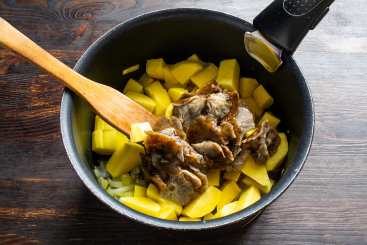 Adding the star ingredient: Frozen opyata mushrooms go directly into the pot for convenience. Adding a block of frozen honey fungus mushrooms (opyata) to the pot with other vegetables.