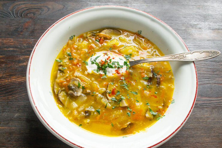A dollop of smetana (sour cream) being added to a bowl of mushroom shchi.