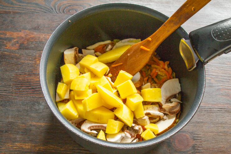 Diced potatoes being added to the pot with other soup ingredients.