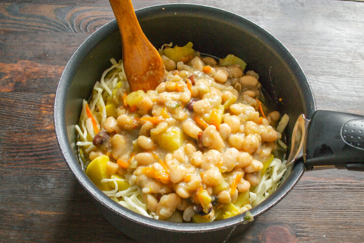 Canned white beans being added to the pot of shchi.