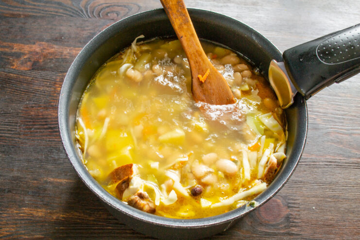 Broth being poured into the pot with vegetables, mushrooms, and beans.