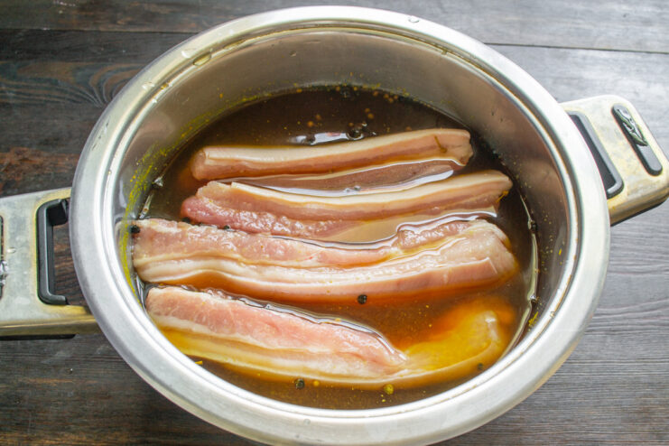 Submerging Pork Belly in the Cooled Brine for Curing Strips of raw pork belly being placed into a pot of dark, spiced brine.
