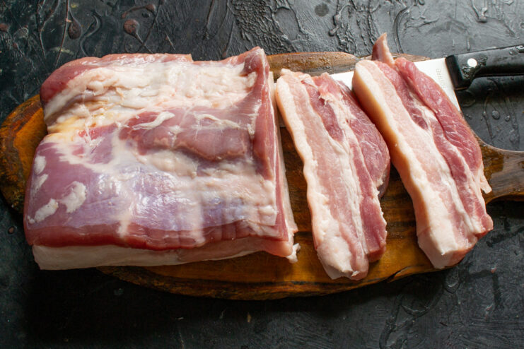 Step 1: Slicing the pork belly into thick pieces. Raw pork belly being sliced into thick, even pieces on a cutting board.