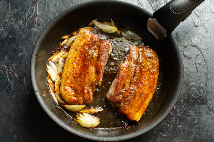 Finishing the glazed pork belly in the oven or under the broiler. The skillet with the glazed pork belly being placed into a hot oven to finish cooking.