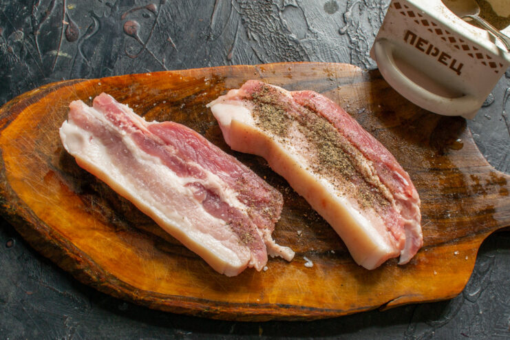 Seasoning the pork belly with salt and pepper. Pieces of raw pork belly being seasoned with coarse salt and freshly ground black pepper.