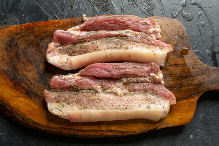 Rubbing thyme and other spices into the pork belly. Seasoned pork belly pieces with dried thyme being rubbed into the meat.