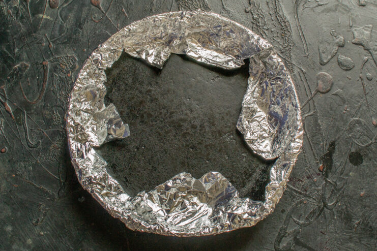Preparing a foil-wrapped skillet to use as a press. A small cast-iron skillet being wrapped in aluminum foil to be used as a weight.