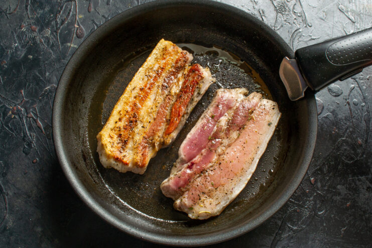 Flipping the pork belly to sear the other side. Flipping the seared pork belly in the skillet to cook the other side, with the weight nearby.