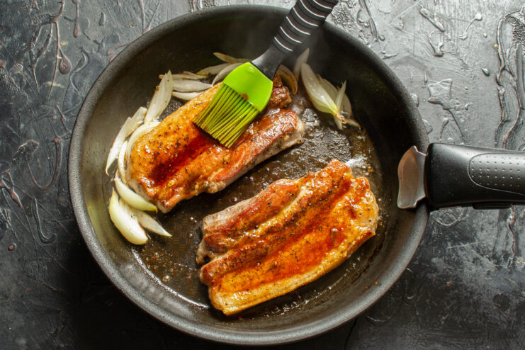 Brushing the seared pork belly with honey glaze. A silicone brush applying a thick honey glaze to the seared pork belly in the skillet.