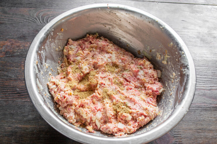 How to Properly Mix Burger Meat by Hand Hands mixing ground beef with other ingredients in a clear bowl to prepare burger patties.