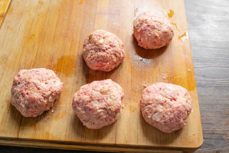 Shaping the Perfect Round Burger Patties Four perfectly formed raw burger patties on a wooden board, ready for cooking.