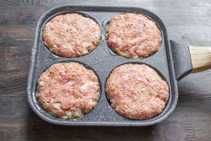 Cooking Burger Patties in a Sectional Pan for Even Results Four burger patties cooking evenly in a black sectional frying pan on the stove.