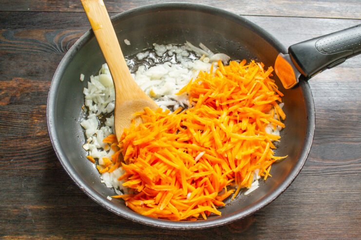 Adding Sweetness and Color - Grated carrots join the onions in the skillet. Grated carrots being added to a skillet with sautéed onions.