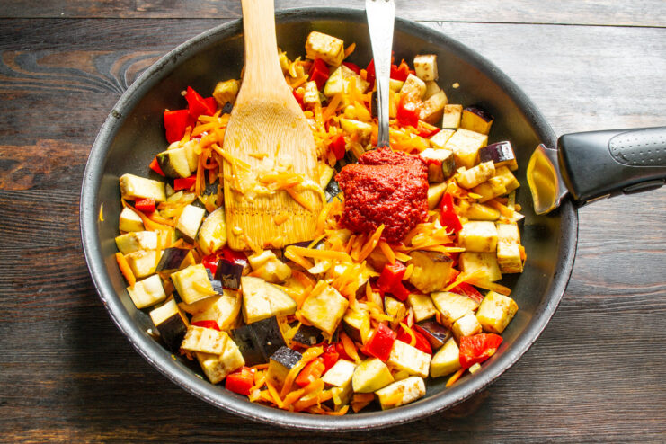 Deepening the Flavor - Adding rich tomato paste to the vegetable mixture. A spoonful of tomato paste being added to the vegetables in the skillet.