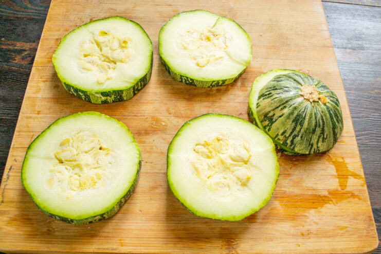 How to prepare zucchini for baking: cutting thick rings. A hand cutting a large zucchini into thick, round slices on a cutting board.