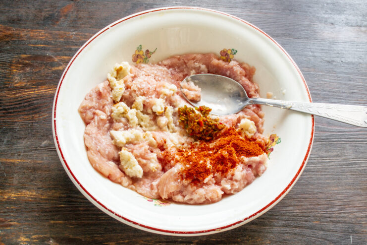 Adding soaked bread to minced meat for a tender filling. Soaked bread being added to a bowl of minced meat to prepare the stuffing.