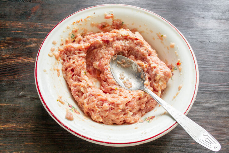 Mixing the minced meat filling until smooth and well-combined. Hands mixing minced meat with bread and spices in a bowl.
