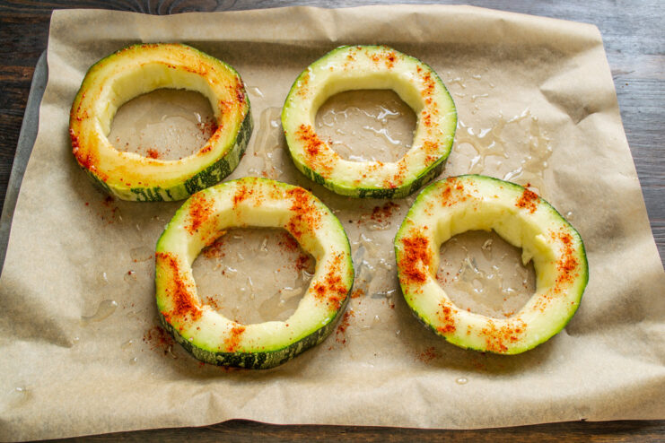 Preparing zucchini rings on a baking sheet before stuffing. Zucchini rings arranged on a baking sheet, being seasoned with oil and salt.