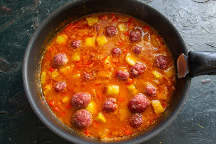 Adding Meatballs to the Simmering Soup Raw meatballs being carefully placed into the simmering vegetable soup.