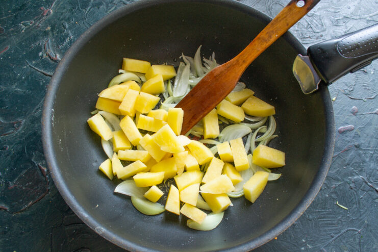 Adding Potatoes to the Sautéed Onions Diced potatoes being added to a pan with sautéed onions.