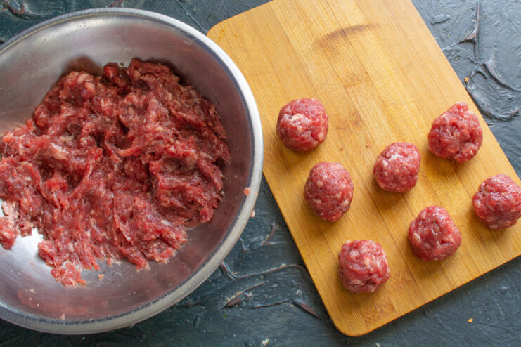 Shaping the Perfect Meatballs for Soup Hands shaping small, uniform meatballs from ground beef mixture on a wooden board.