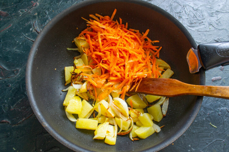 Grating Carrots for the Soup Base A hand grating a peeled carrot on a coarse box grater.