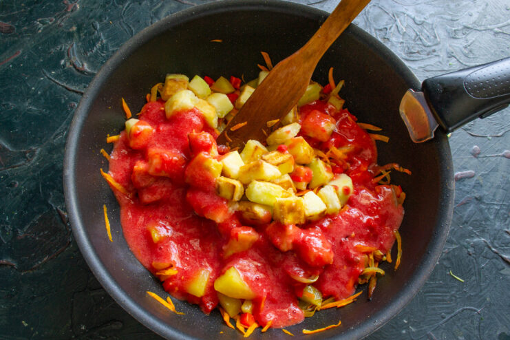 Incorporating Tomato Puree into the Vegetable Base Fresh tomato puree being poured into a pan with sautéed vegetables.