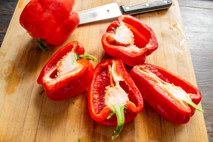 Step 1: How to Cut Bell Peppers for Freezing A hand cutting a red bell pepper in half lengthwise on a cutting board.