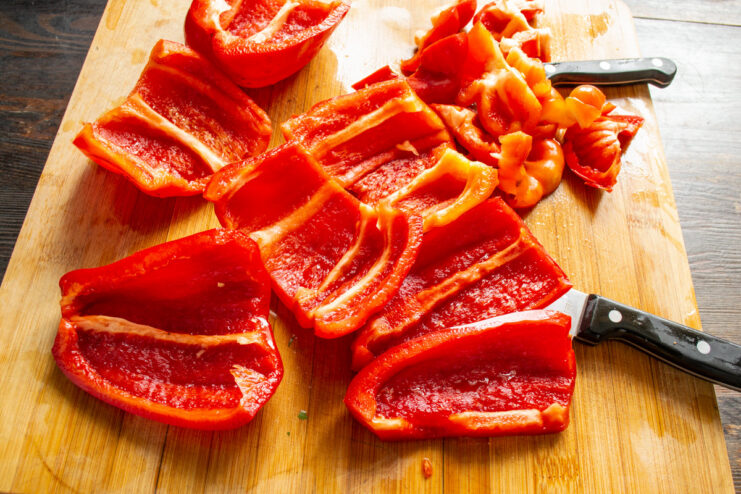 Removing Seeds and Membranes from Bell Peppers A hand using a sharp knife to remove the white membranes from inside a red bell pepper half.