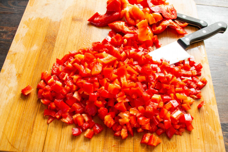 How to Dice Bell Peppers for Freezing Dicing red bell pepper strips into small cubes on a white cutting board.
