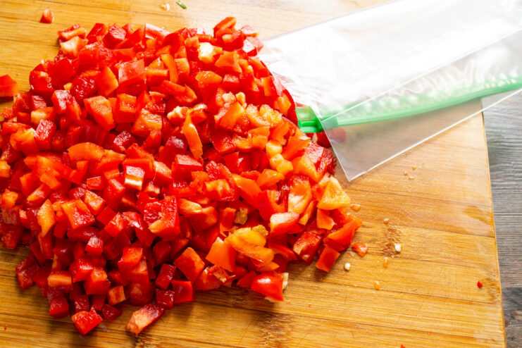 Using Freezer Bags for Storing Bell Peppers A pile of diced red bell peppers next to a clear freezer-safe zipper bag.