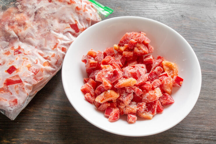How to Use Frozen Bell Peppers in Your Cooking A person taking a portion of frozen diced bell peppers from a large freezer bag.