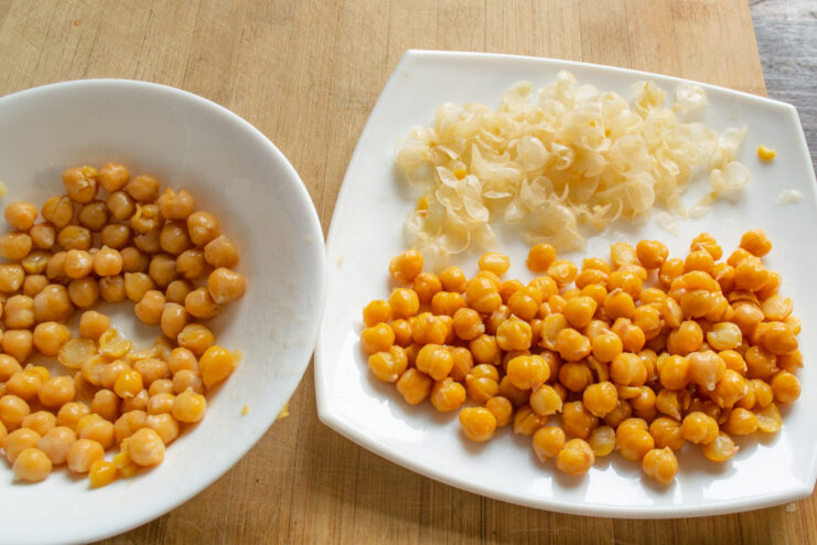 Removing the cooked chickpeas from the pot to cool down. Cooked chickpeas spread out on a white plate, ready for peeling.