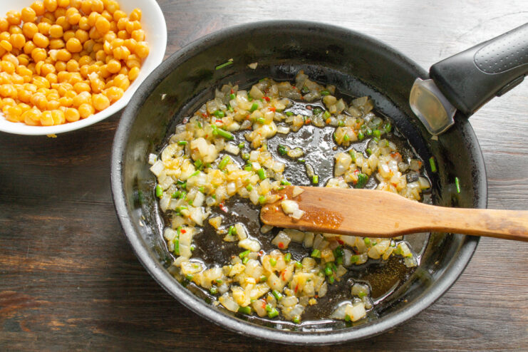 Sautéing the vegetables and spices until the onion is soft and translucent. Onions, garlic, and celery being sautéed in a pan with spices.