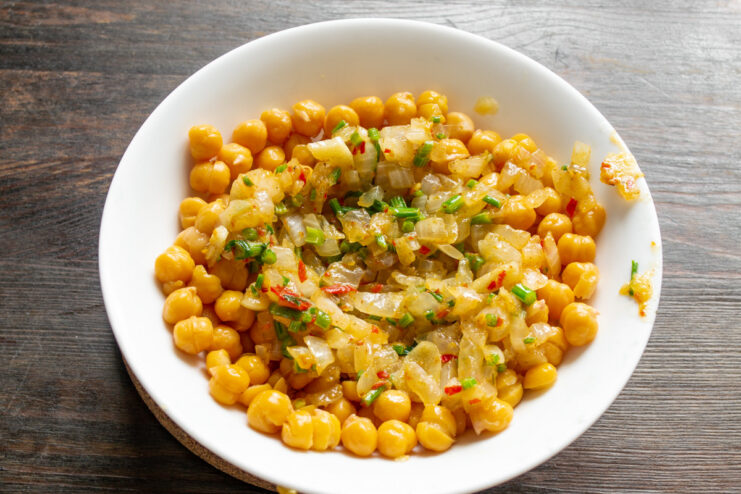 Combining the sautéed vegetables with the cooked chickpeas. A bowl of peeled chickpeas with sautéed onions and celery on top.