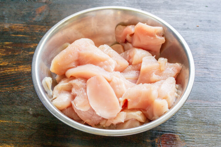 Preparing chicken breast for grinding into meatballs. Raw chicken breast cut into cubes on a cutting board, ready for the meat grinder.