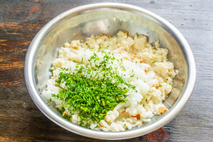 Adding fresh dill for an aromatic touch to the tefteli. A bowl with soaked bread, diced onion, and freshly chopped dill.